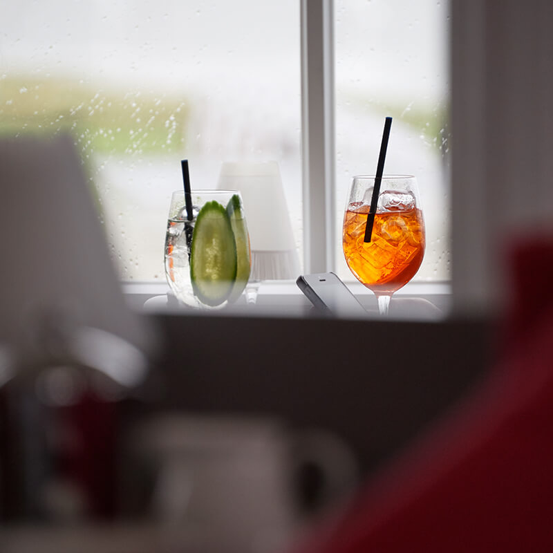 Stimmungsbild mit bunten Drinks vor verregneter Scheibe.